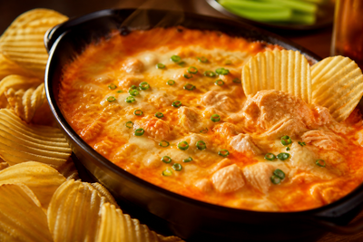 Bubbling buffalo chicken dip in a cast-iron dish with ridged potato chips